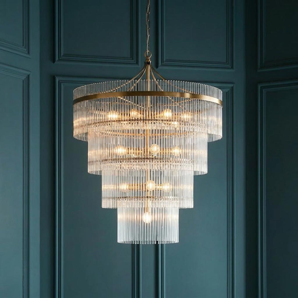 A four-tiered Marietta Brass chandelier with vertical glass rods hanging against a dark teal paneled wall.