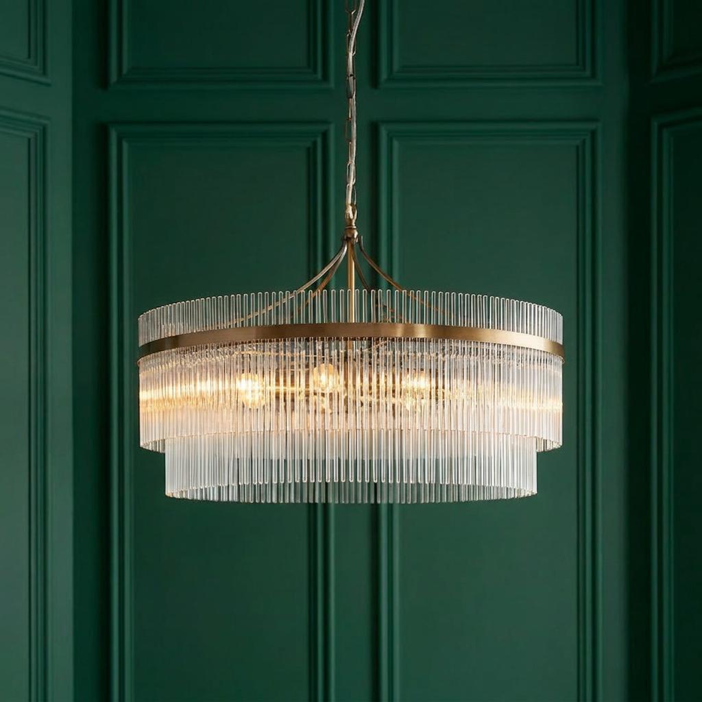 Tiered brass ceiling pendant with vertical glass rods illuminated against a dark green paneled wall.