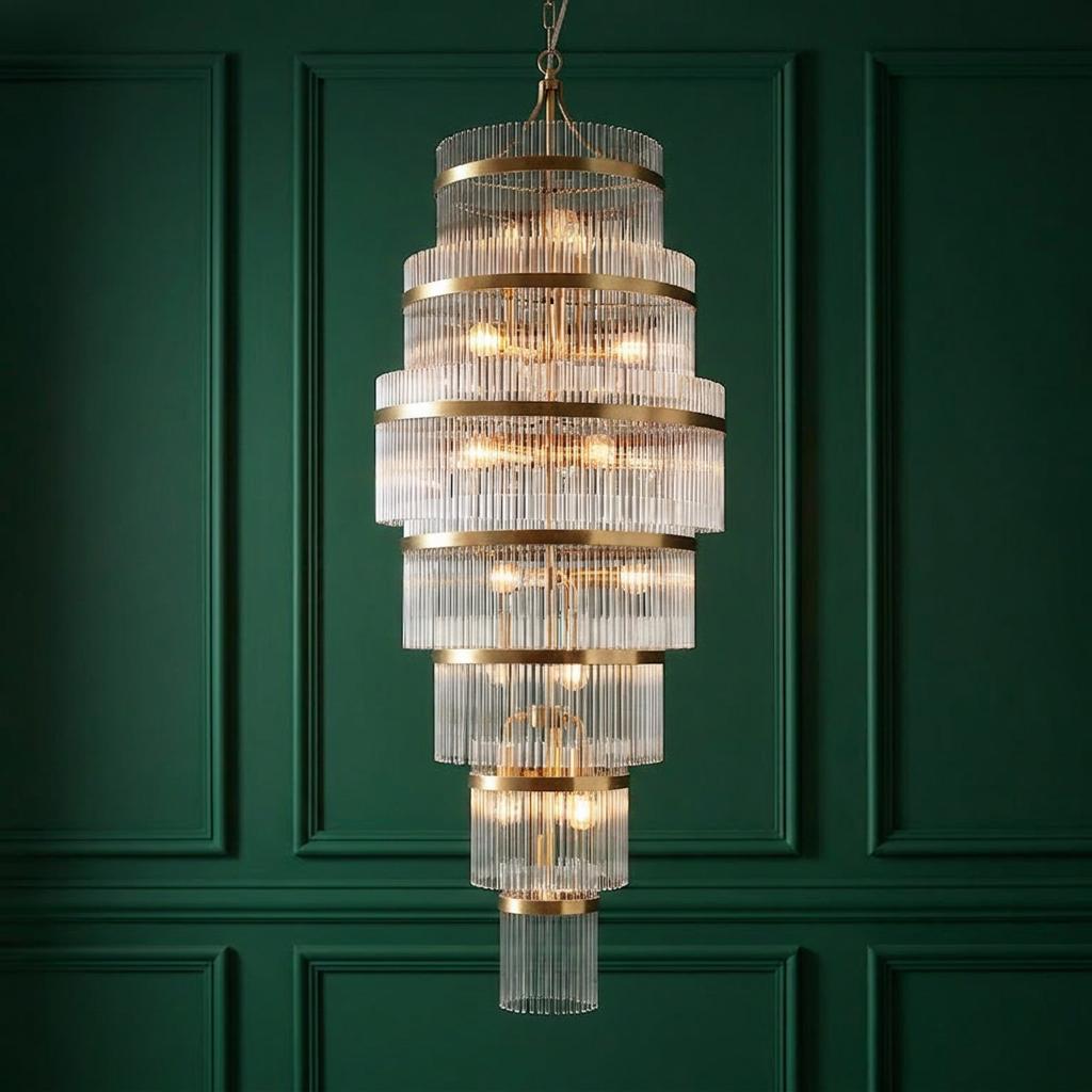 A multi-tiered brass and glass rod chandelier hanging against a dark green paneled wall.