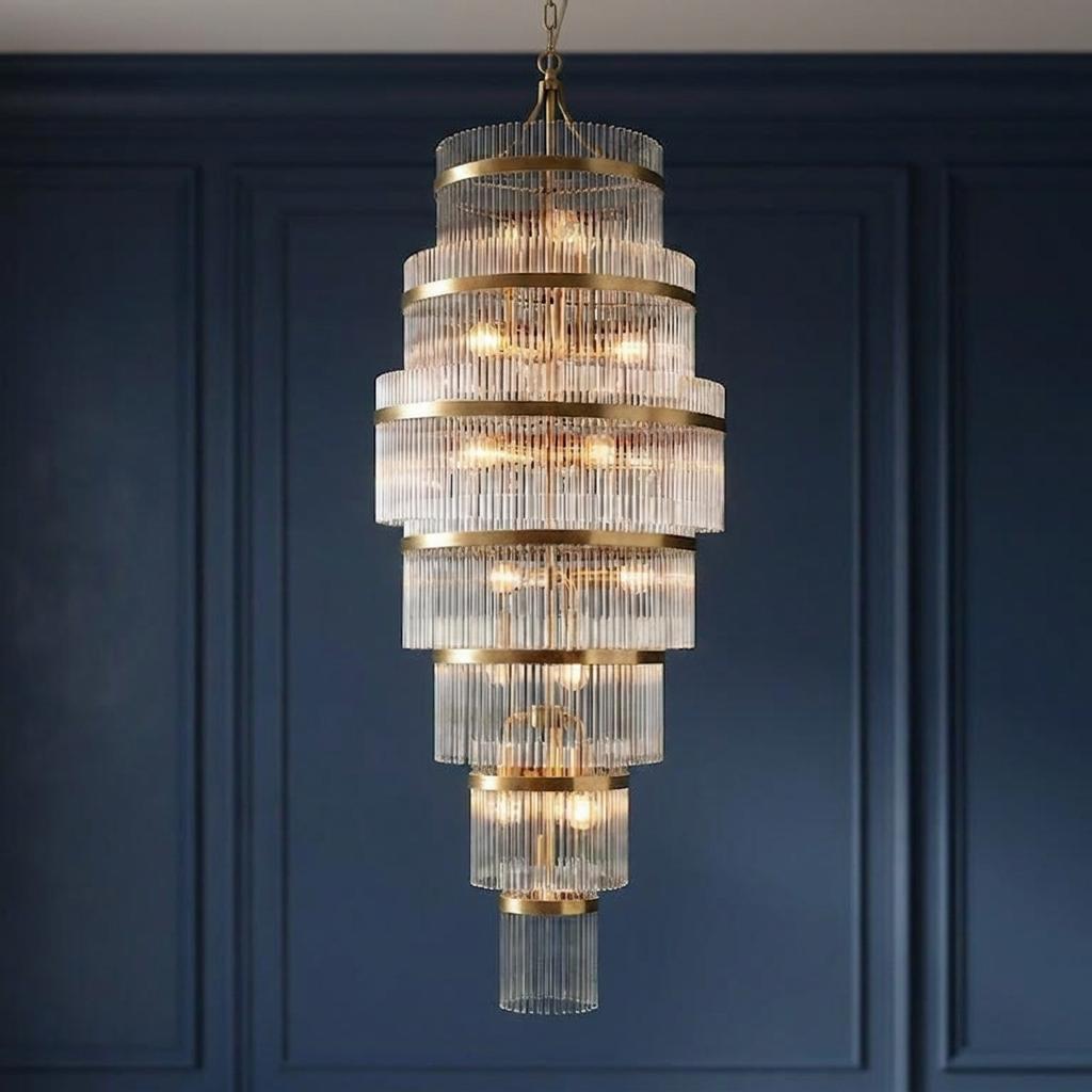 Eight-tiered brass and glass rod chandelier illuminated against a dark blue paneled wall.