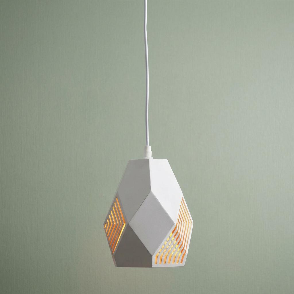 Geometric white pendant light with laser-cut slits glowing gold against a pale green wall.