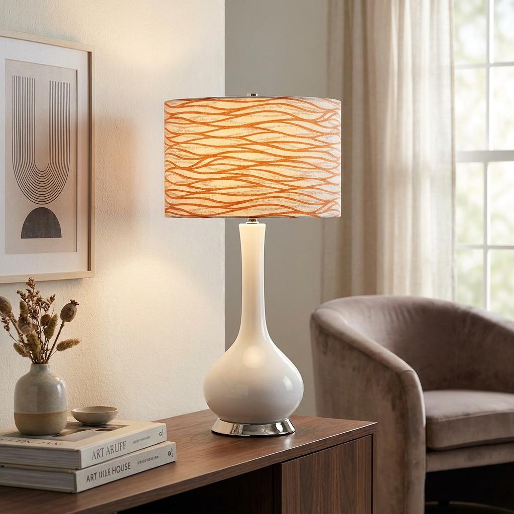 White ceramic table lamp with a pink wavy pattern shade on a wooden sideboard in a light-filled living room.