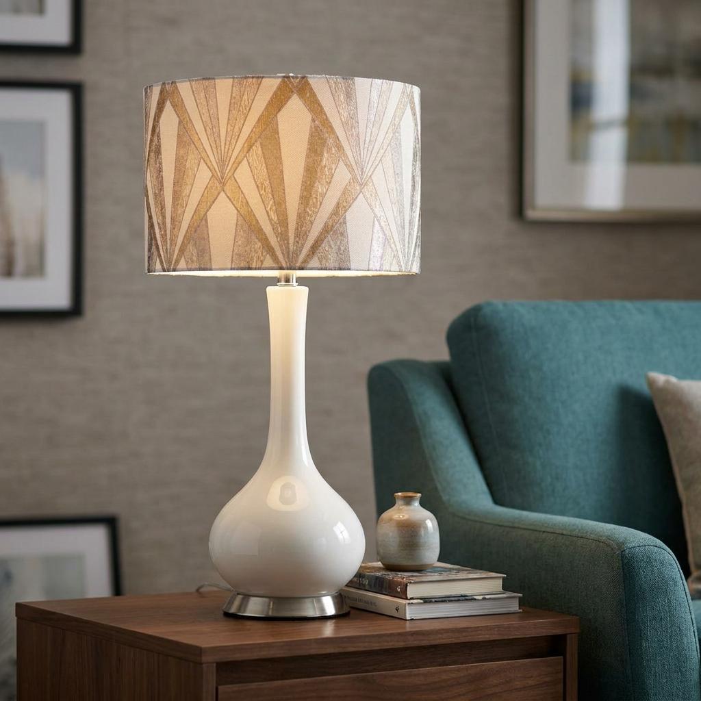White ceramic table lamp with a silver geometric patterned shade on a wooden side table next to a teal chair.