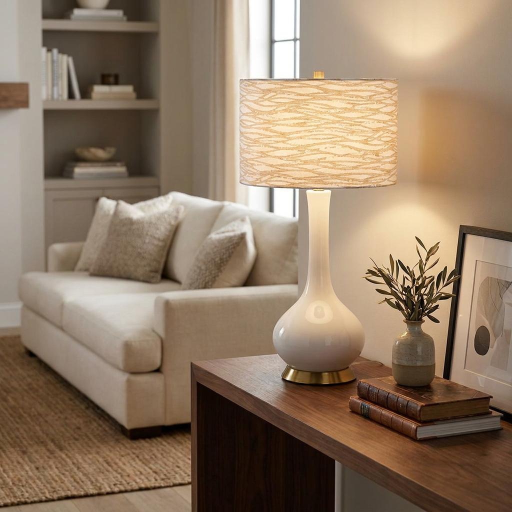 White ceramic teardrop table lamp with a patterned drum shade on a wooden console in a cozy living room.
