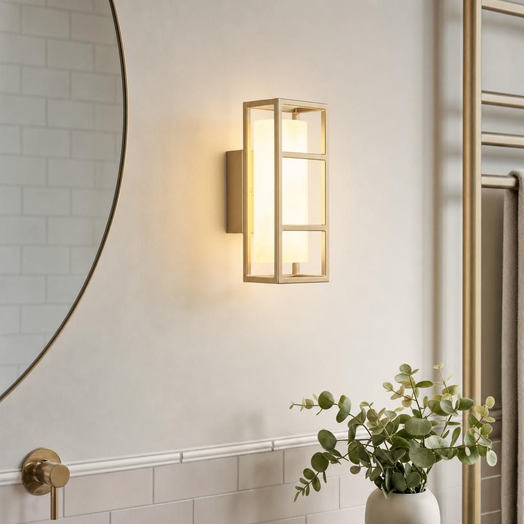 Rectangular matt gold wall light with frosted diffuser glowing beside a mirror in a modern bathroom.