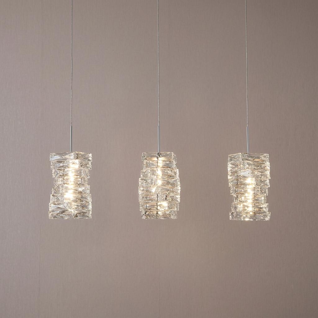 Trio of modern chrome and clear textured glass pendant lights glowing against a neutral wall.