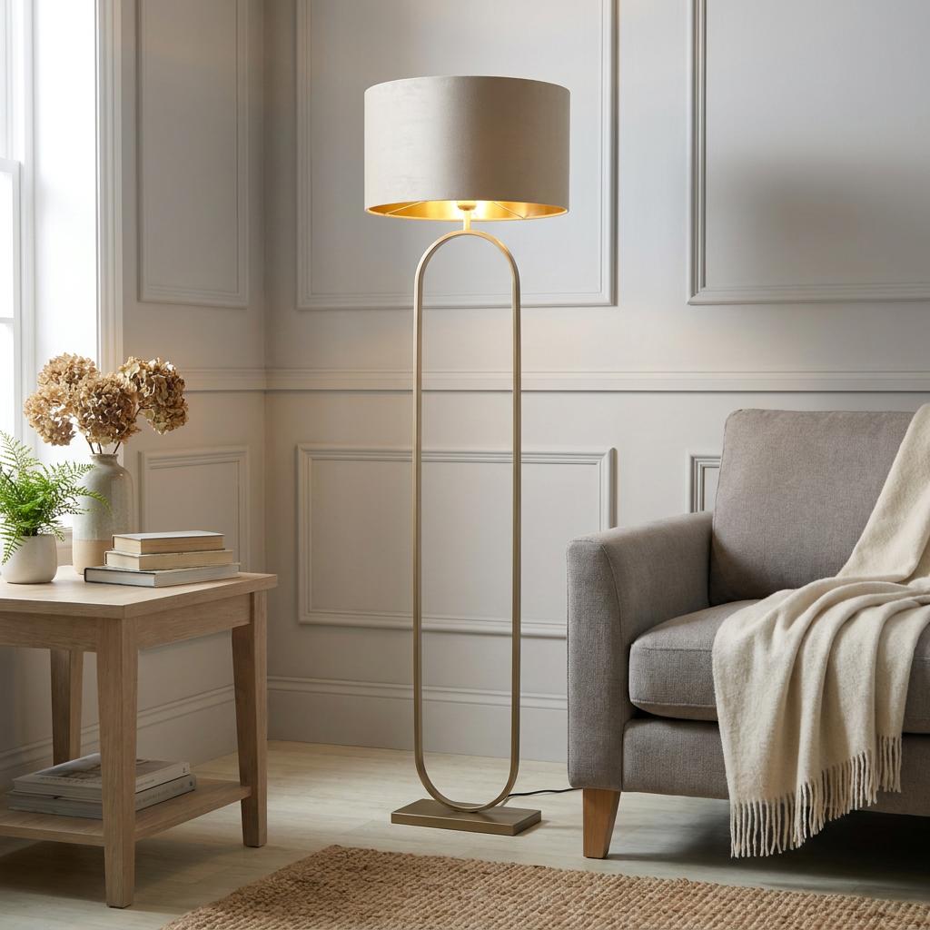 Bronze floor lamp with an open pill-shaped frame and taupe velvet shade in a neutral living room corner.