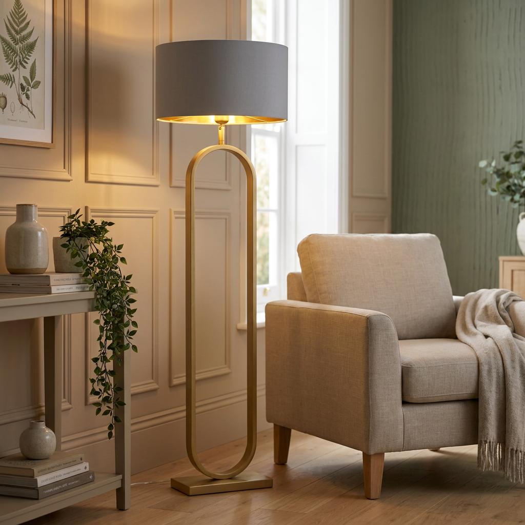 Bronze floor lamp with an oval base and grey velvet shade next to a beige armchair in a warm living room.