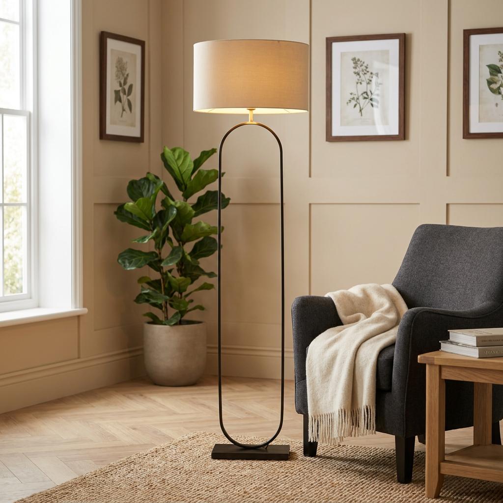 Modish matte black floor lamp with a taupe velvet shade standing in a cozy living room next to a dark armchair.