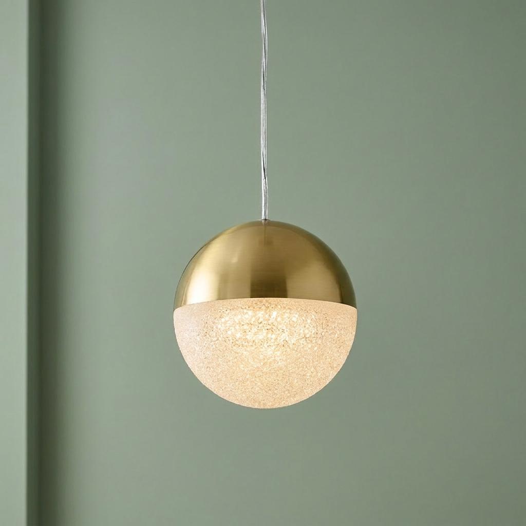 A spherical pendant light with a gold top and glowing textured glass bottom hangs against a pale green wall.