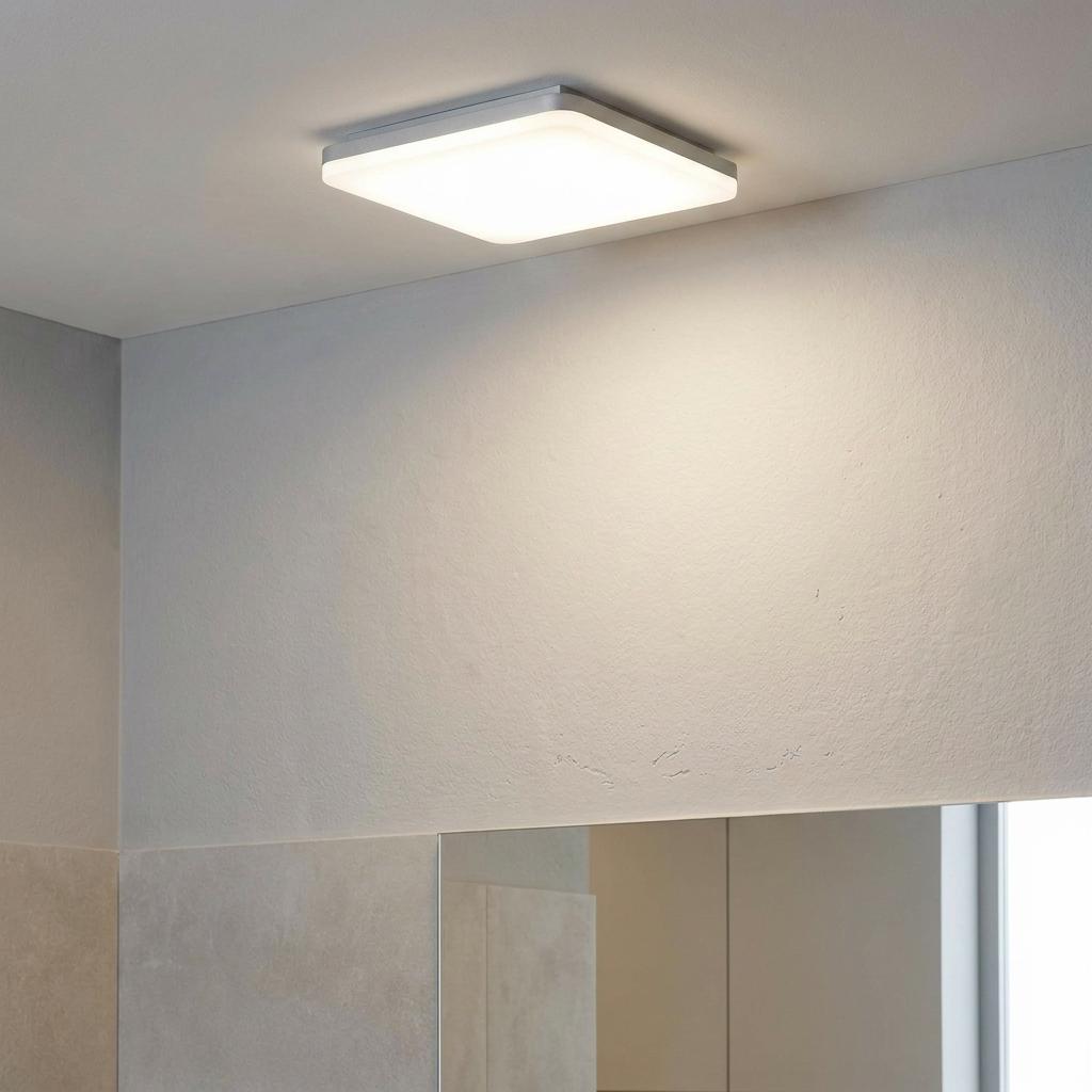 Modern square white LED flush ceiling light illuminating a bathroom wall above a mirror.