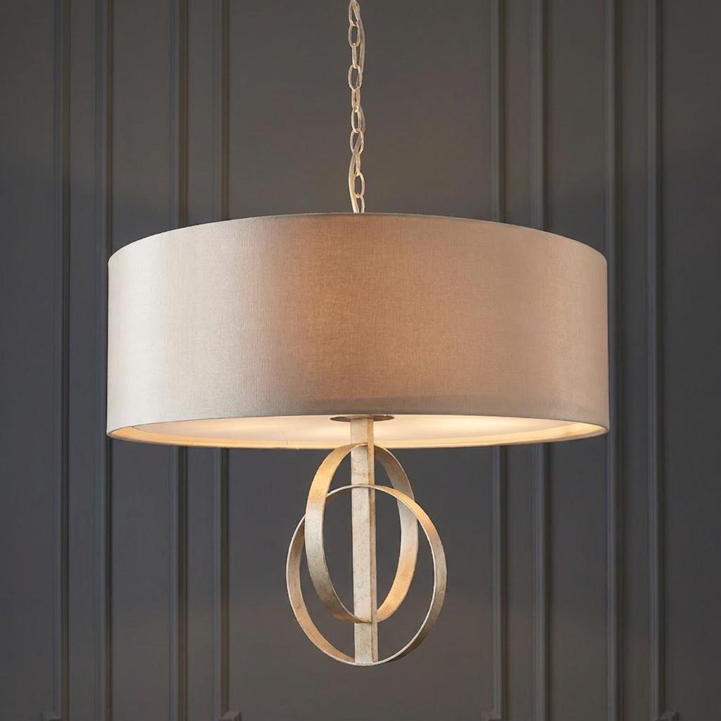 Silver leaf pendant light with a mink drum shade and interlocking metal rings against a dark paneled wall.