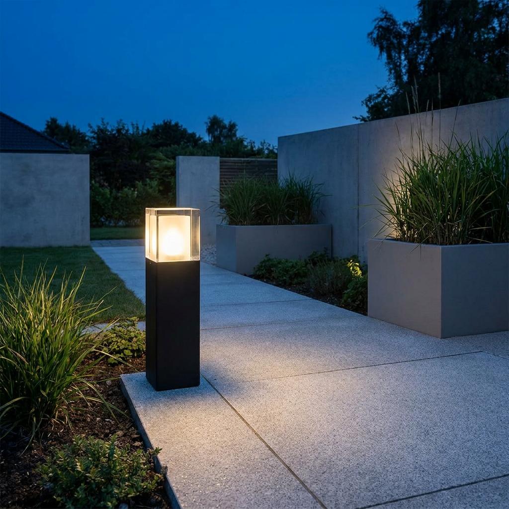Black square outdoor bollard with clear top illuminating a modern stone path at dusk.
