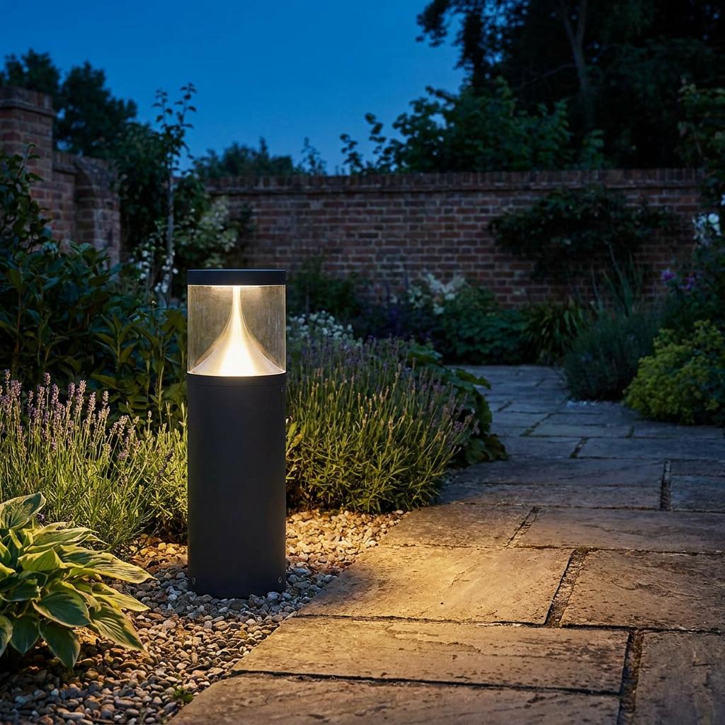 A graphite outdoor bollard light illuminating a stone garden path and lavender at dusk.