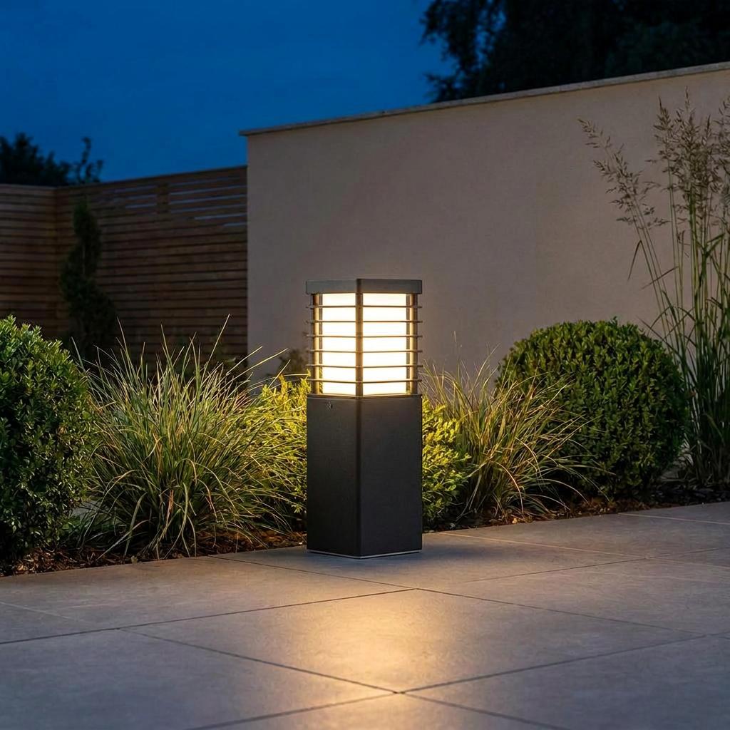 Modern black bollard light illuminating a tiled garden patio and shrubs at dusk.