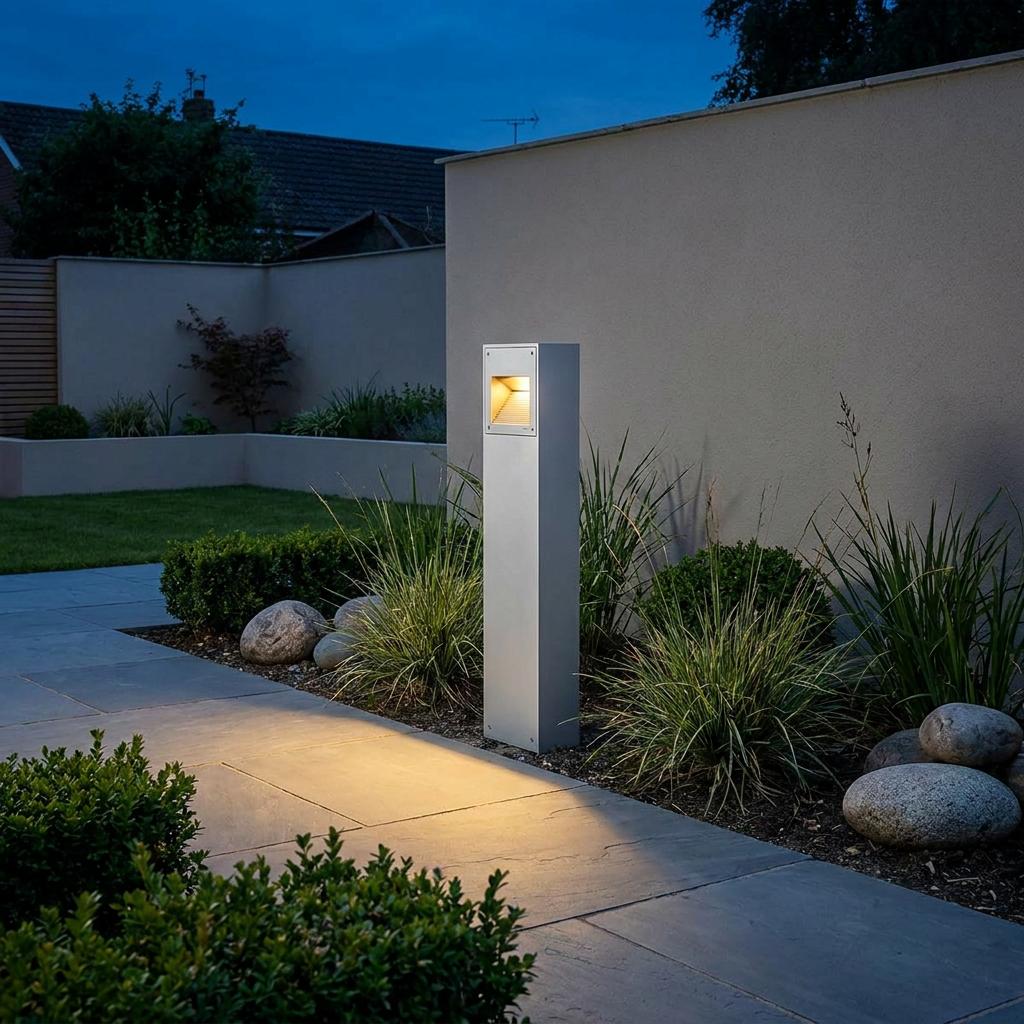 Norlys Namsos LED tall aluminium bollard light casting warm light on a stone pathway in a modern garden.