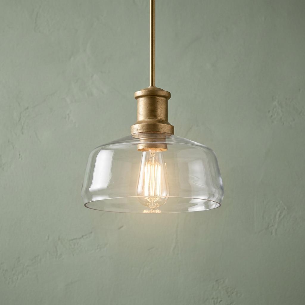 Brass duo-mount pendant light with a clear blown glass shade and Edison bulb against a textured green wall.