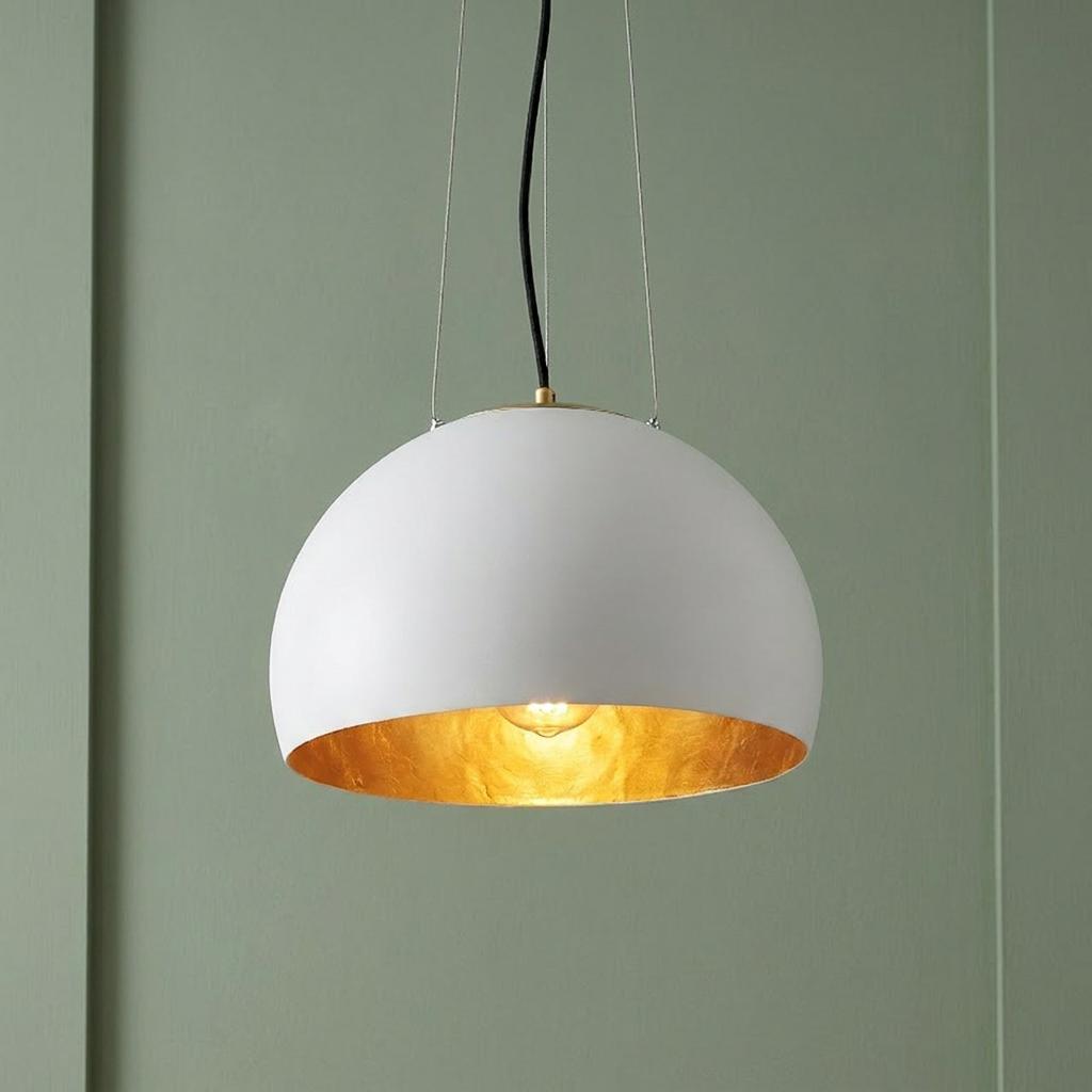 White dome pendant light with a gold leaf interior suspended against a sage green paneled wall.