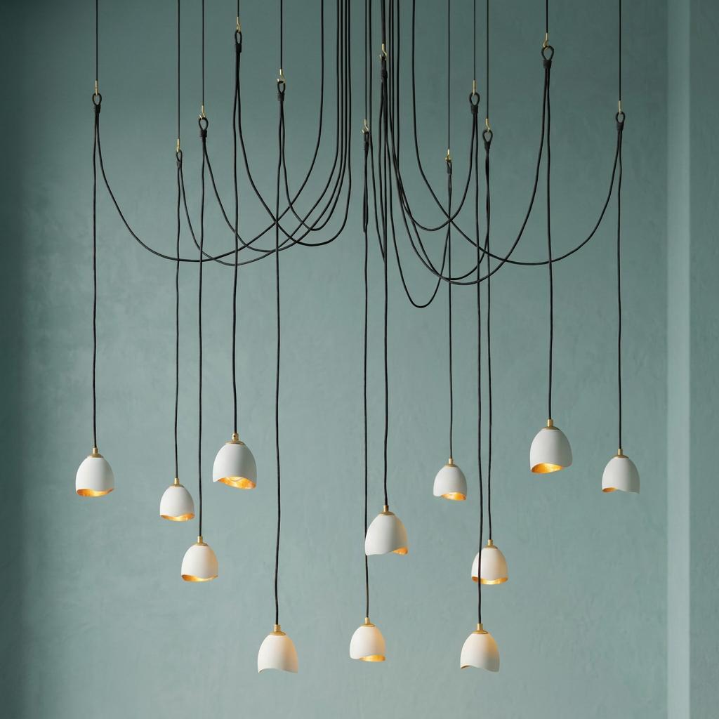 Modern multi-light pendant with small white bells featuring gold interiors and draped black cords.