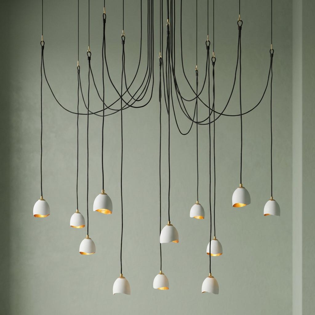 Modern 12-light pendant with white and gold shades suspended by draped black cords against a sage green background.
