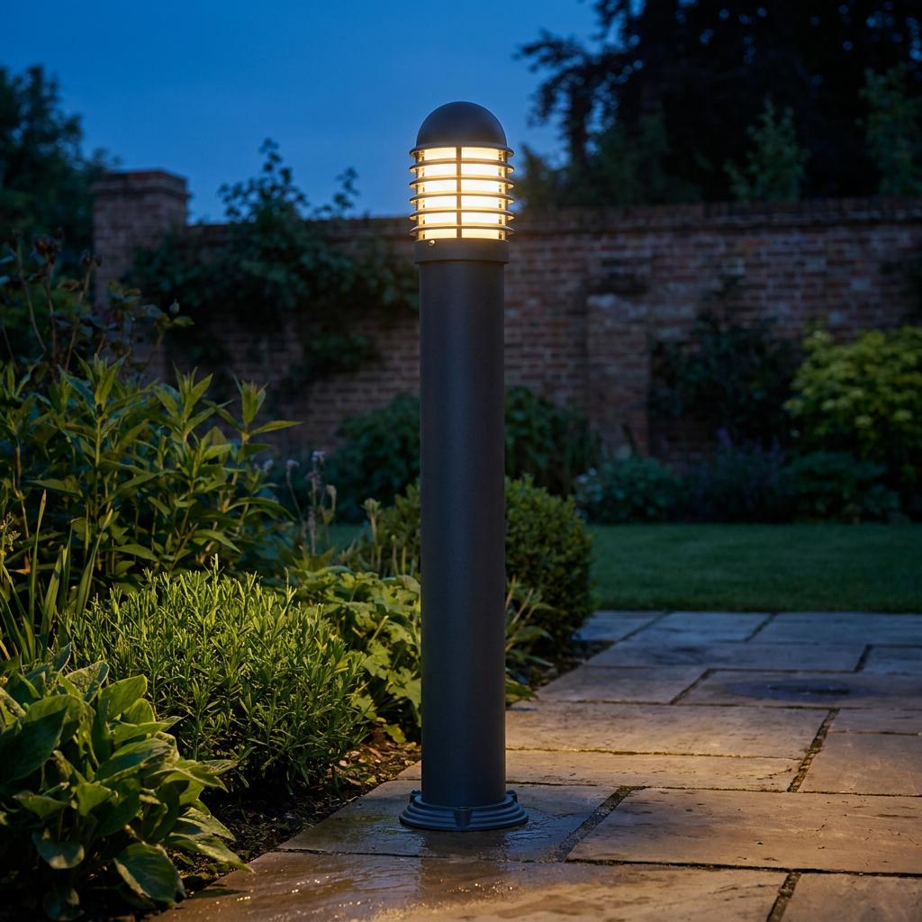 Black outdoor bollard light illuminating a stone pathway in a lush garden at twilight.
