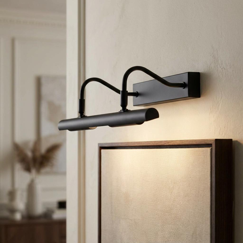 Black double-arm picture light mounted on a neutral wall, illuminating framed canvas artwork with a warm glow.