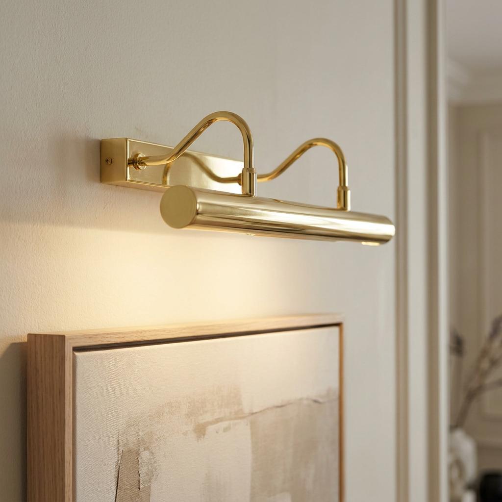 Polished brass double-arm picture light illuminating a framed painting on a neutral wall.