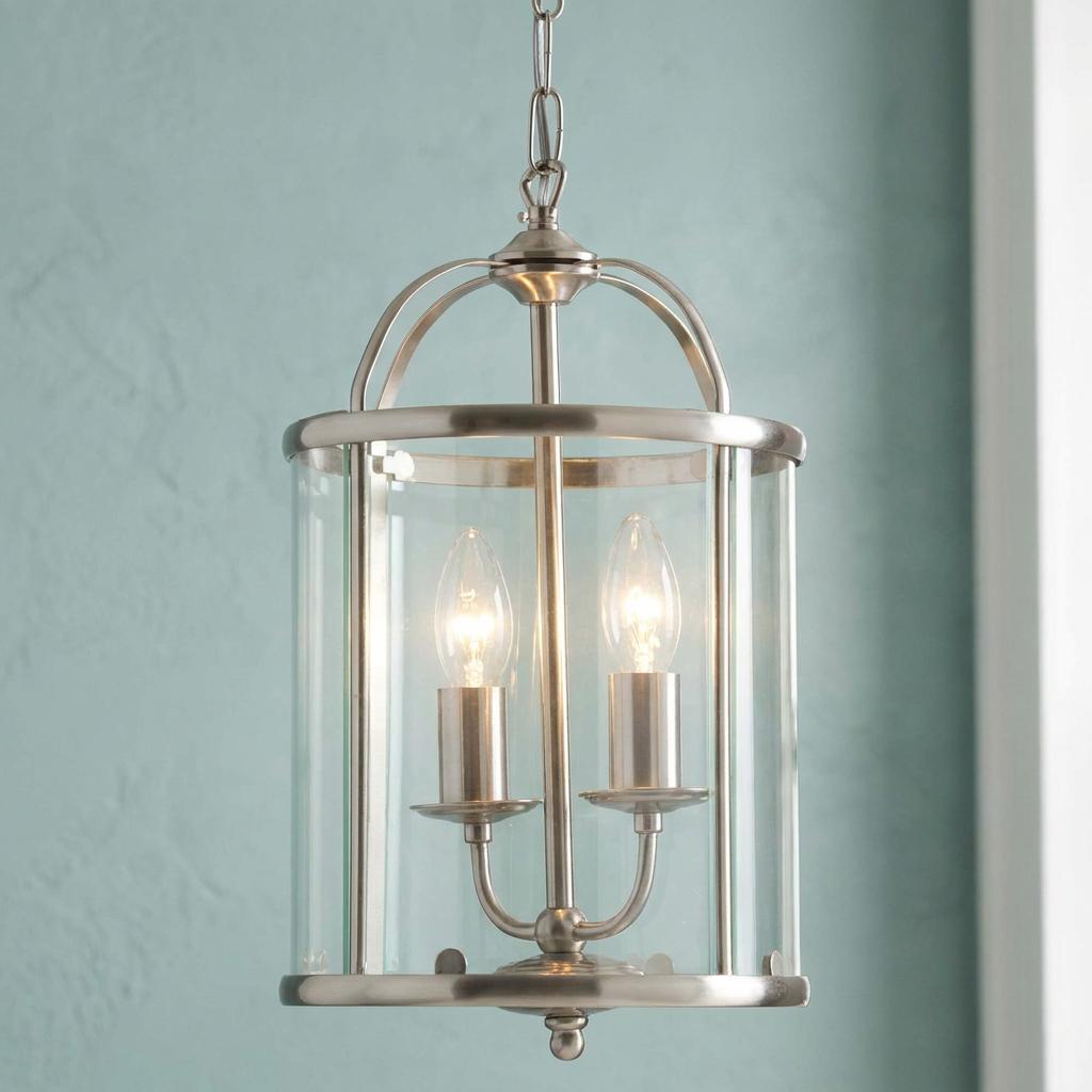 Antique chrome two-light ceiling lantern with a clear glass shade lit against a pale blue wall.