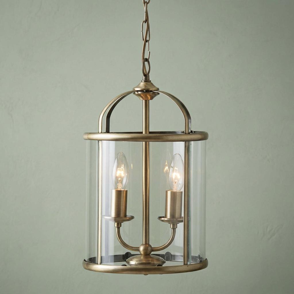 Two-light antique brass lantern ceiling light with clear cylindrical glass housing.