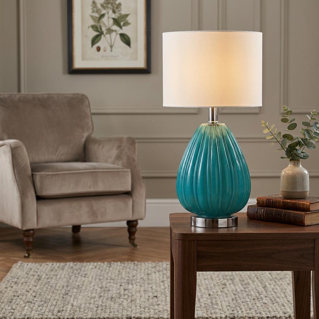 Teal ribbed glass table lamp with a white drum shade on a wooden side table in a living room.