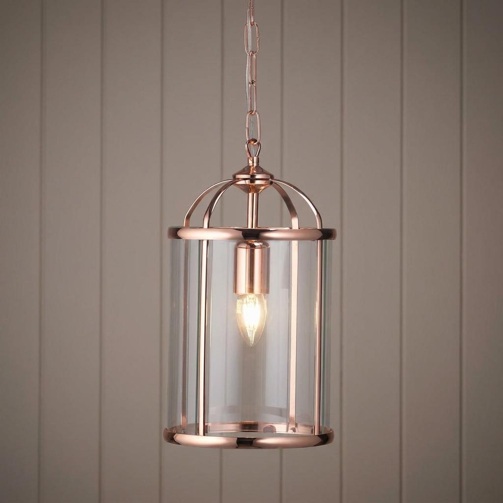 Elegant copper ceiling lantern with a clear glass cylinder and lit bulb against wood paneling.