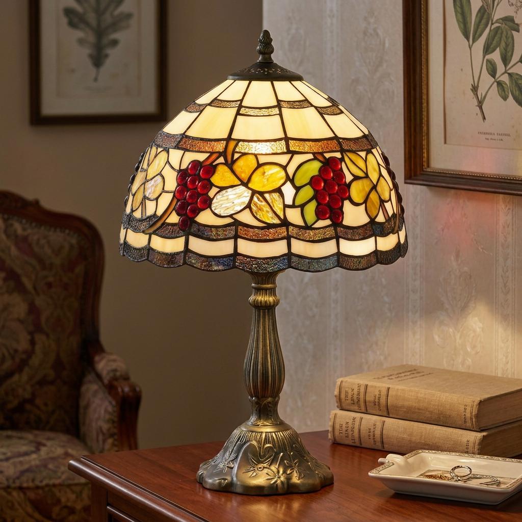 Tiffany table lamp with a stained glass grape design on a bronze base, lit on a wooden table with books.