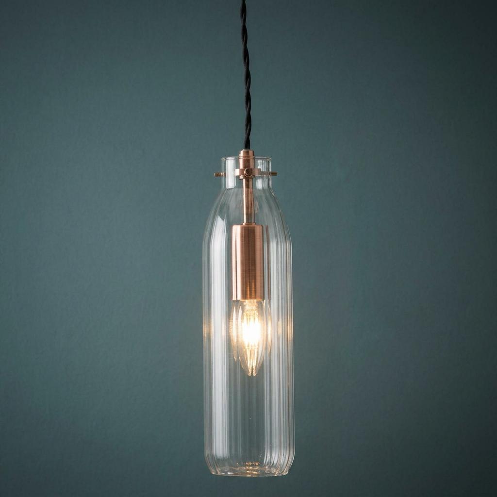 Copper and ribbed glass bottle pendant light hanging against a dark teal wall.