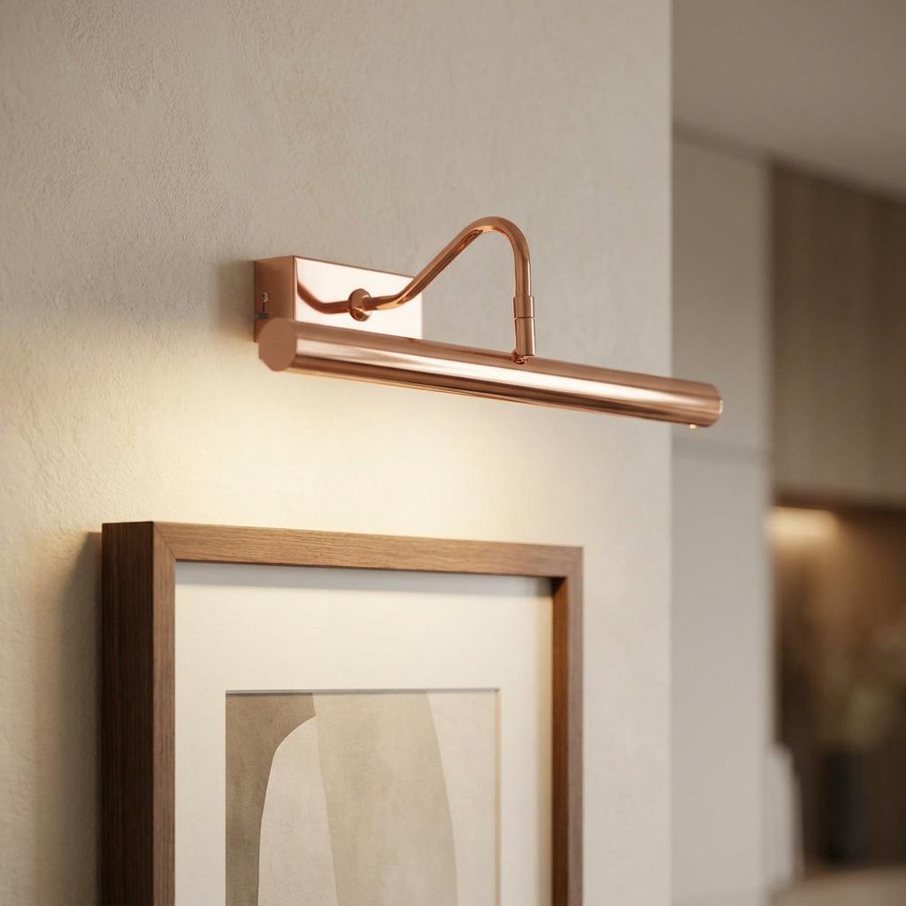 Polished copper LED picture light with a warm white glow mounted on a wall above a framed artwork.