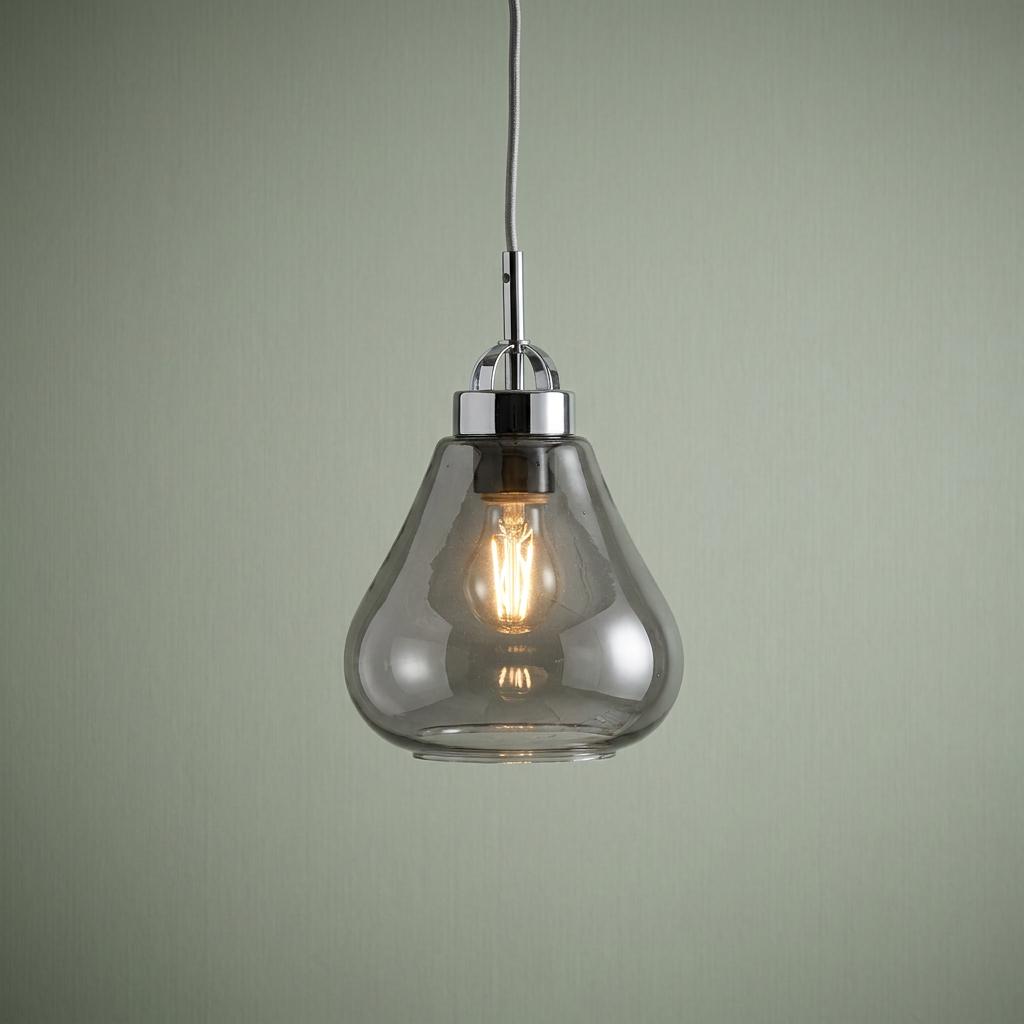 Chrome pendant light with a teardrop-shaped glass shade and glowing filament bulb against a pale green wall.
