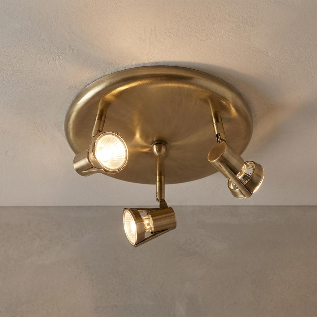 Antique brass 3-light spotlight fixture mounted on a ceiling and illuminated.