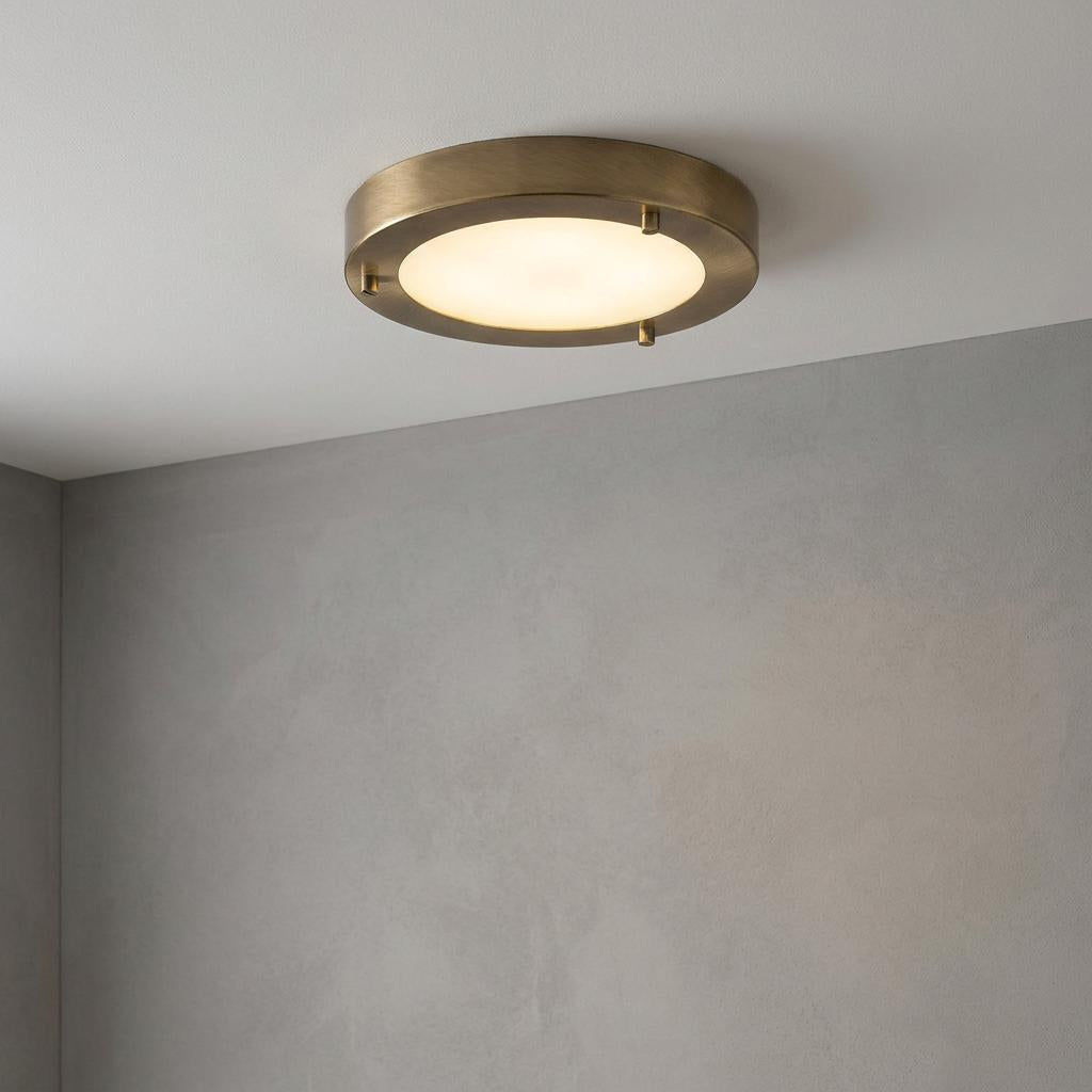 Small antique brass flush bathroom ceiling light with frosted glass mounted on a white ceiling.