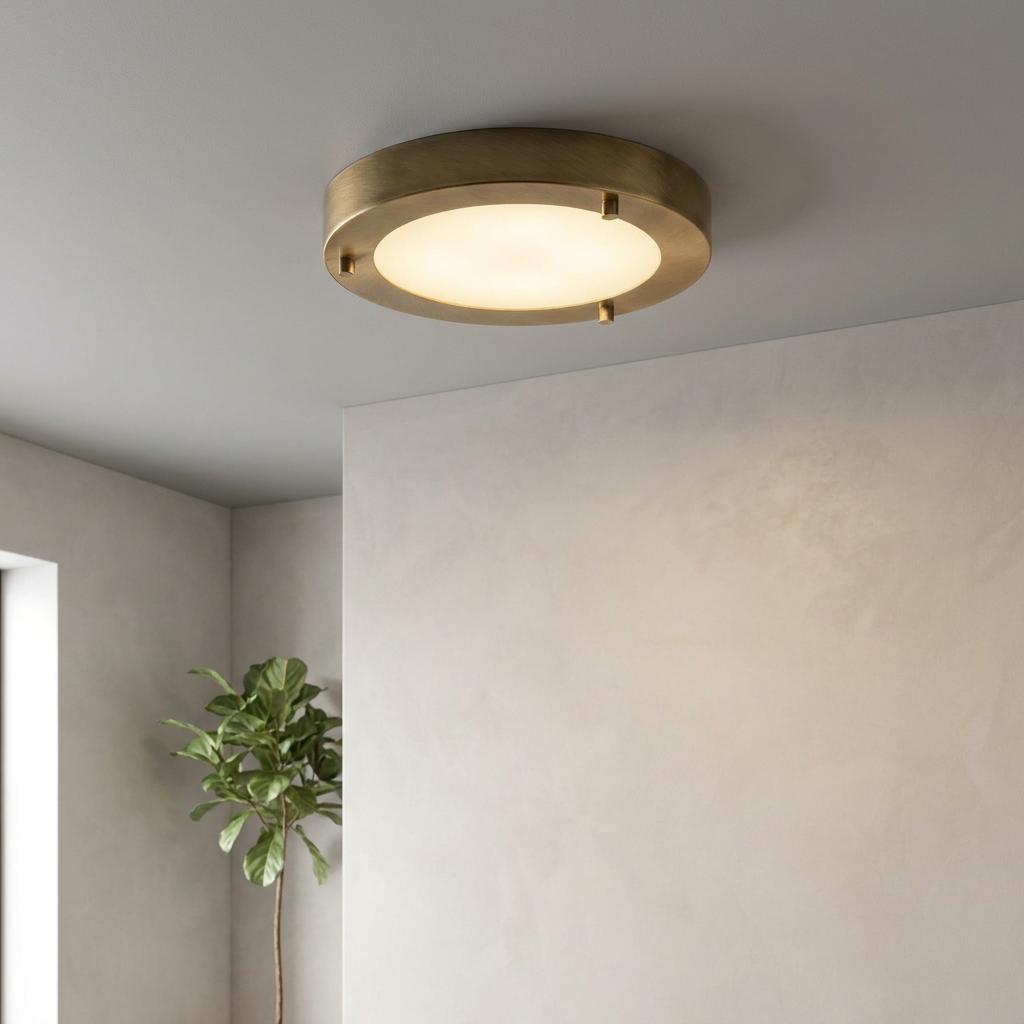 Antique brass circular flush ceiling light with a warm glowing diffuser mounted on a neutral ceiling.