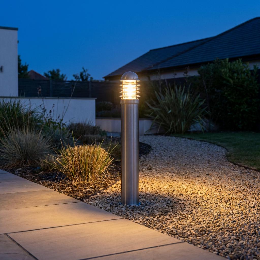 Lit stainless steel bollard light brightening a gravel pathway and garden at twilight.