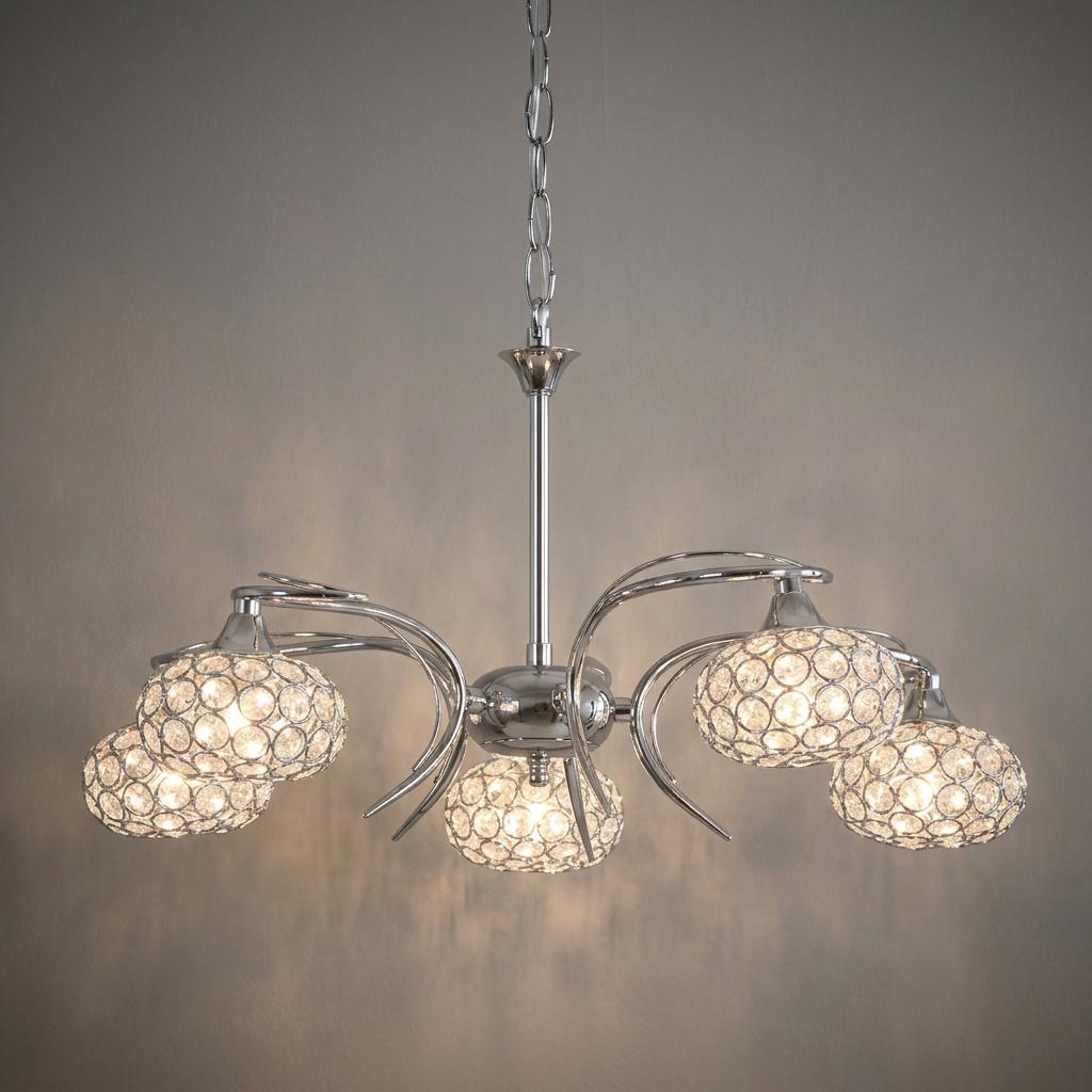 Five-light chrome chandelier with curved arms and sparkling crystal-beaded shades glowing against a neutral wall.