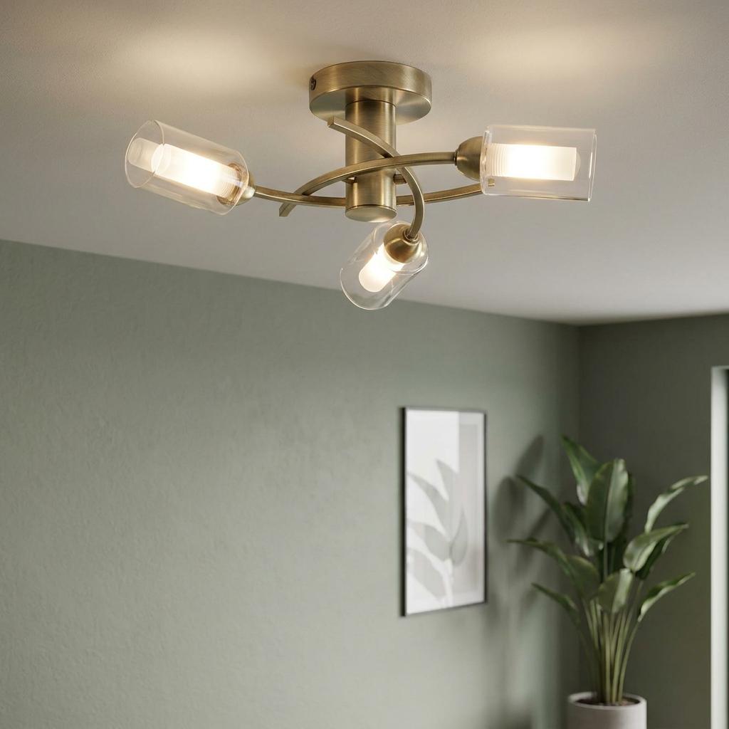 Three-light antique brass flush ceiling light with curved arms and clear glass shades against a green wall.