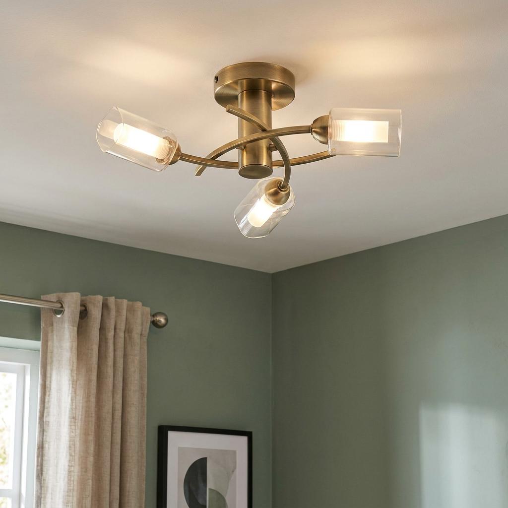 Ofira 3-light antique brass flush ceiling fixture with clear glass shades mounted in a green-walled room.