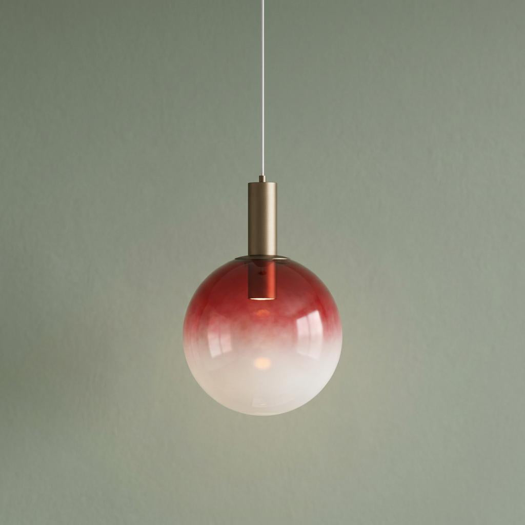 Red ombre glass globe pendant light with latte metal hardware hanging against a muted green wall.