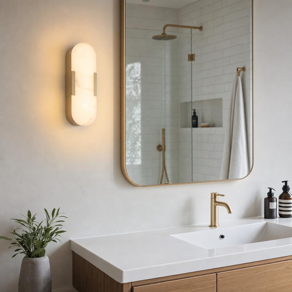 Modern oval opaline wall sconce with matt gold brackets mounted in a minimalist bathroom beside a large mirror.