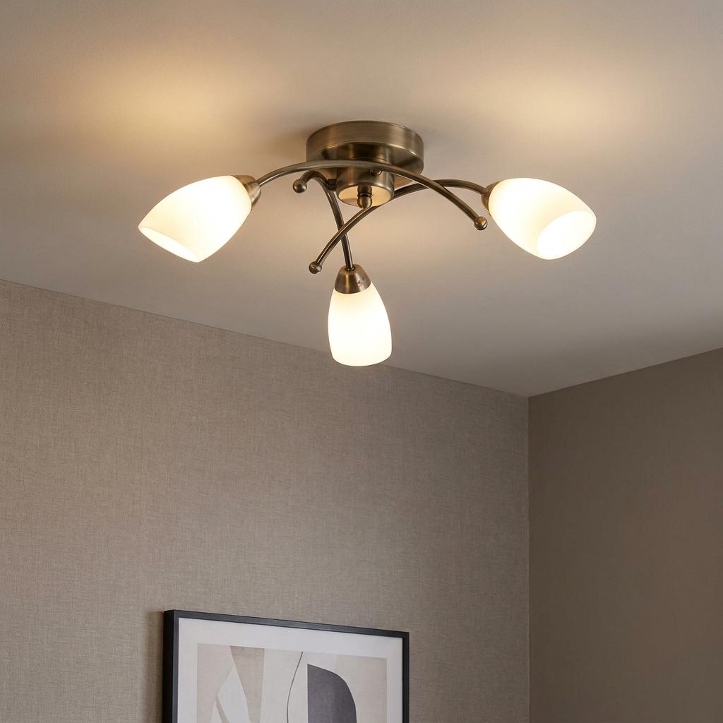 A brass semi-flush ceiling light with three curved arms and opal glass shades illuminated in a room.