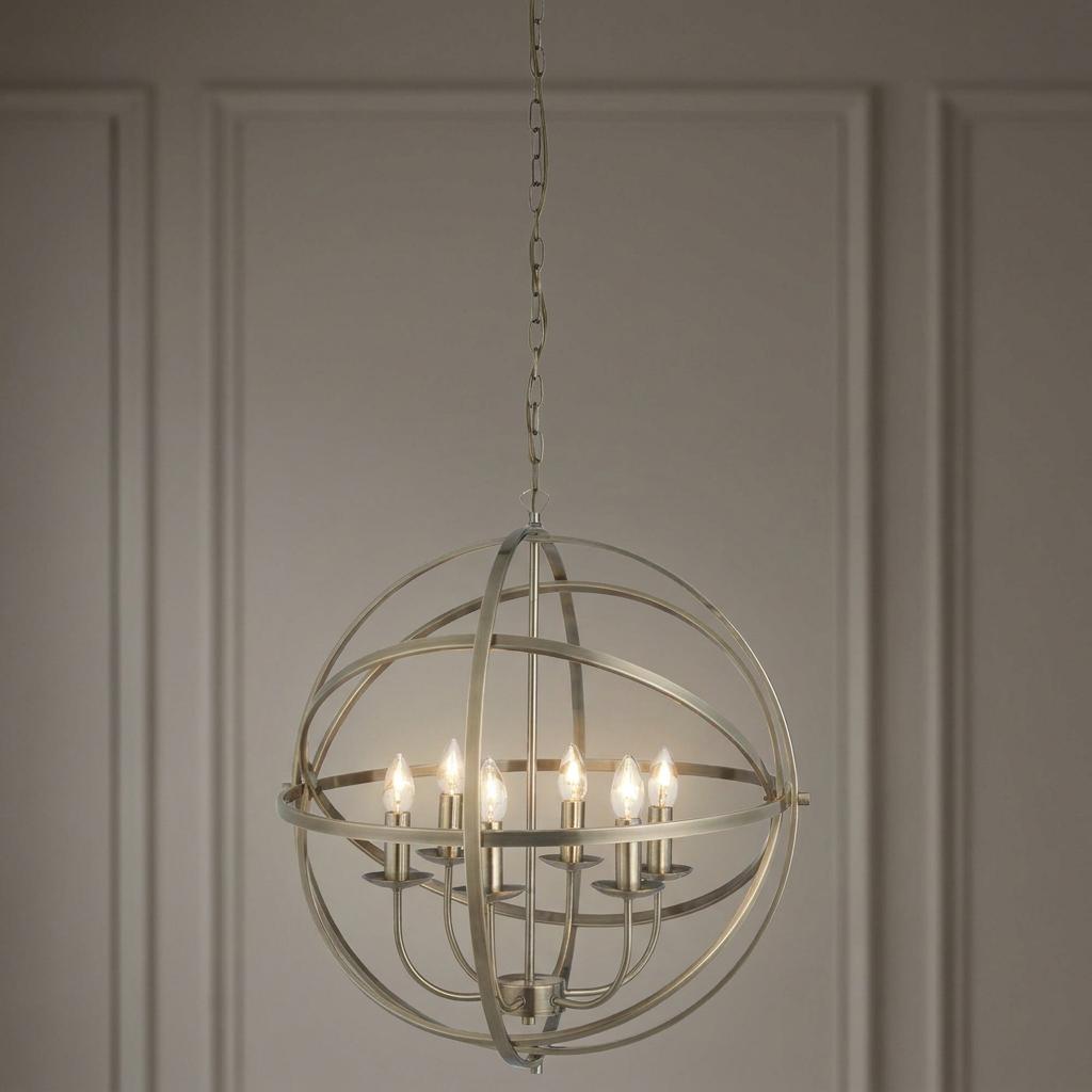 A 6-light antique brass orb pendant chandelier with a cage frame hanging in front of a paneled wall.