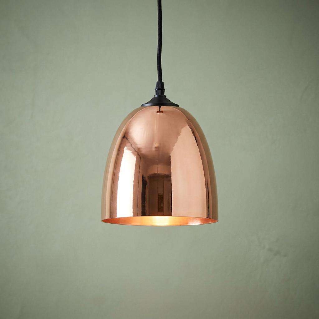 Dome-shaped copper glass pendant light with a warm glow, suspended against a soft green textured wall.
