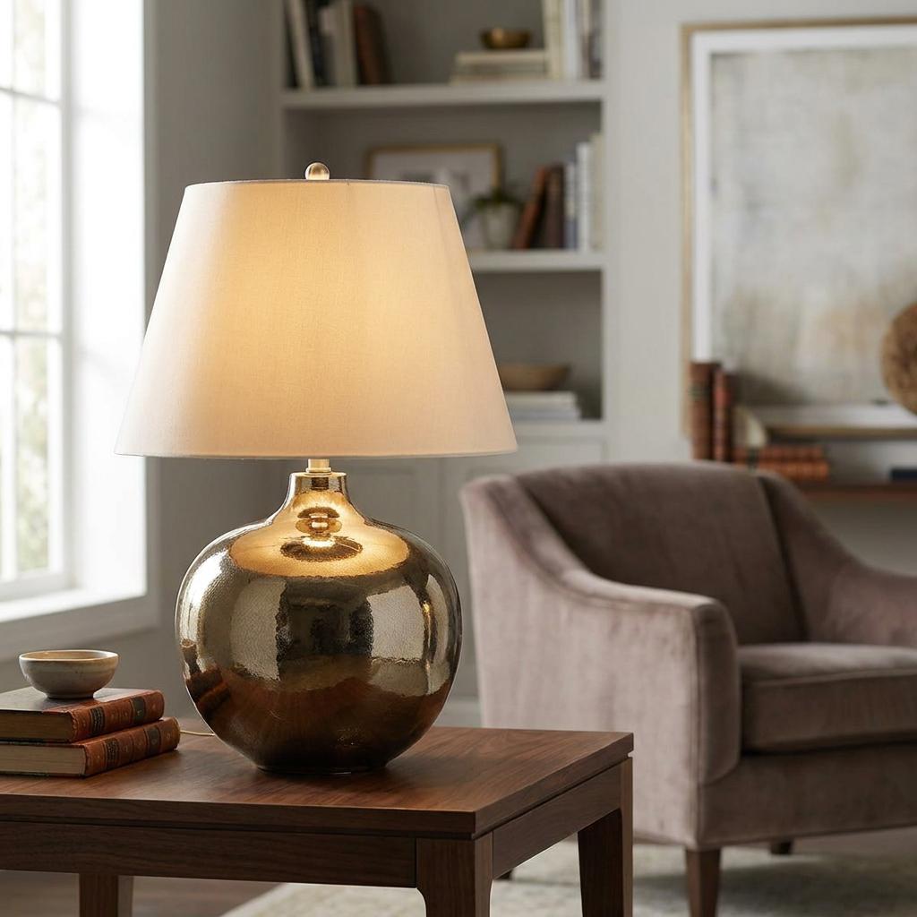 Ottoman Ceramic Table Lamp with a hammered gold base and ivory shade on a wooden table in a living room.