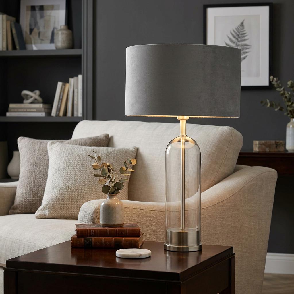 Oxford table lamp featuring a clear glass base and grey velvet shade, placed on a side table in a living room.