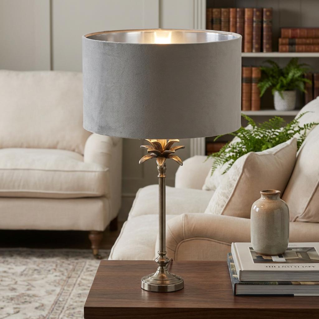 Antique nickel palm tree table lamp with a grey velvet shade on a wooden side table in a living room.